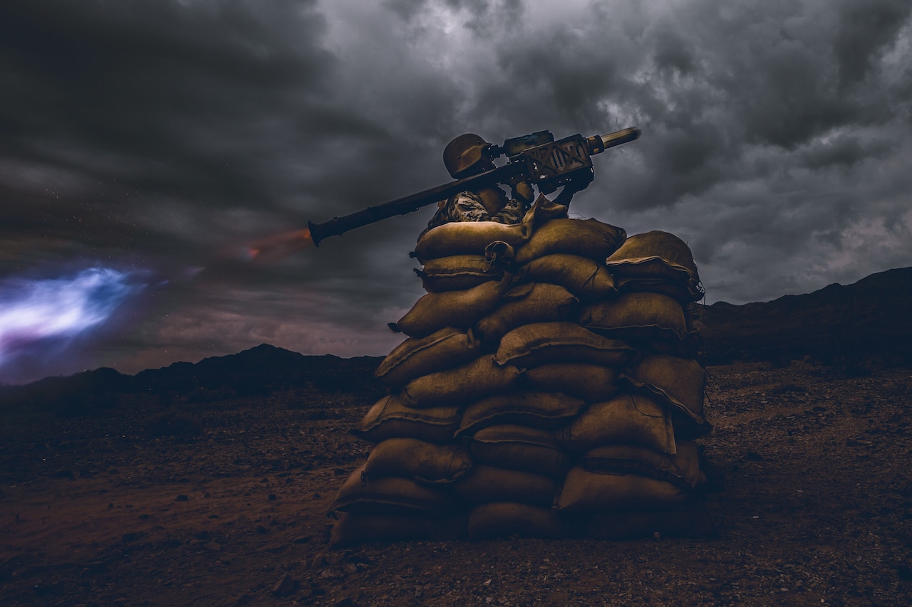 Atop a stack of sandbags, a Marine launches a shoulder-mounted projectile.