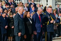 The president, vice president, Secretary of Veterans Affairs, and commanding general are all bowing in prayer during a ceremony. The general has removed his hat. Behind these four people is a large audience who are also participating in the ceremony.