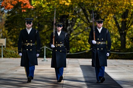Three members of the Army's Old Guard unit are marching toward the photographer. They are wearing dark overcoats, hats and sunglasses, and the two on the right are carrying rifles on their right shoulders.
