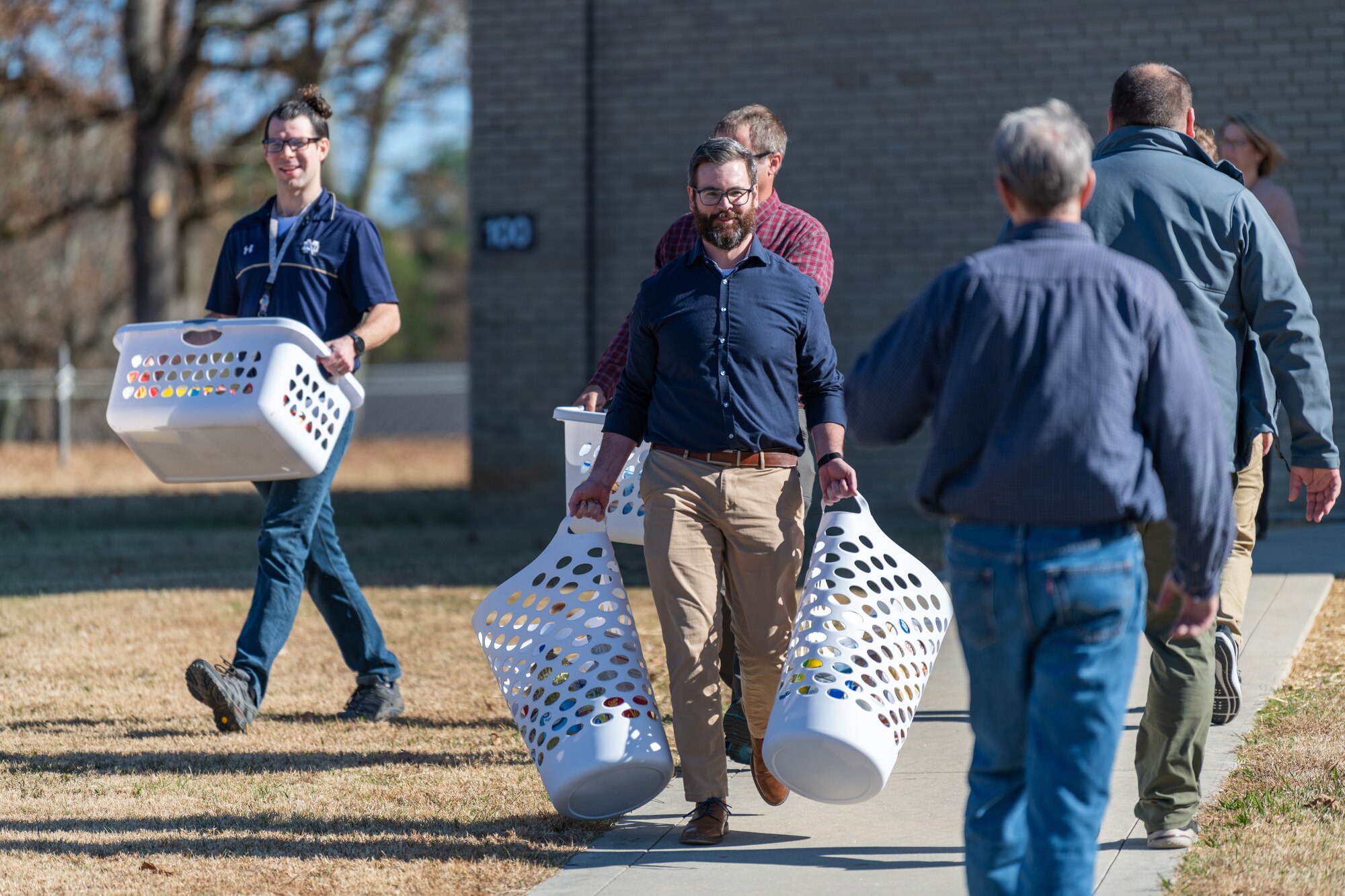 Arnold Air Force Base team members carry baskets assembled during the Arnold AFB Junior Force Council Thanksgiving Food Basket Drive to load for distribution Nov. 16, 2023, at Arnold Air Force Base, Tenn. The drive took place over a week in November. During the effort, Arnold AFB team members donated nonperishable food items to be used for the baskets. This year, 57 baskets were provided for Coffee County families in need of food to prepare Thanksgiving meals. Team members pictured include Adam Moon, center, and Joseph Bedell, left. (U.S. Air Force photo by Keith Thornburgh)