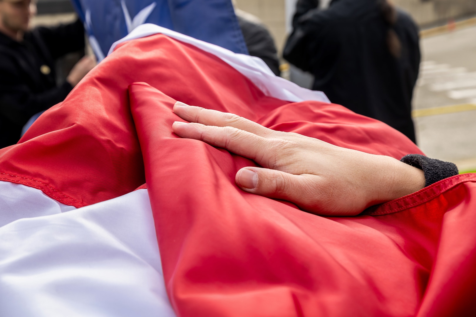 A Sailor's hand helps secure the new American flag as it's unfurled Nov. 9, 2023, during a special Veterans Day flag-replacement ceremony near the State Street Gate Entrance at Puget Sound Naval Shipyard & Intermediate Maintenance Facility in Bremerton, Wash. (U.S. Navy photo by Ben Hutto)