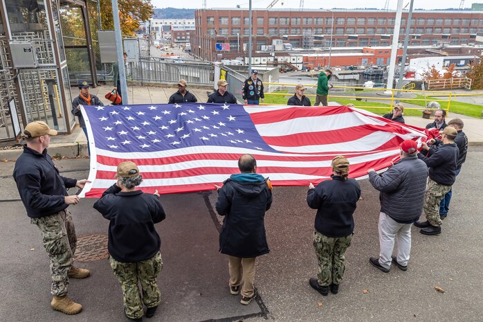 A group of PSNS & IMF Sailors and military veterans prepare to hoist a new American flag near the State Street Gate Entrance at Puget Sound Naval Shipyard & Intermediate Maintenance Facility in Bremerton, Wash. Nov. 9, 2023, during a special Veterans Day flag-replacement ceremony hosted by the Veterans Employee Resource Group. (U.S. Navy photo by Ben Hutto)