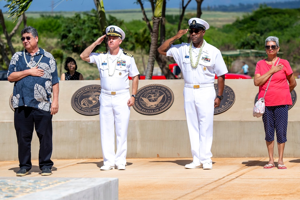 Commanding Officer and Senior Chief, in dress white uniforms, salute while two civilians place hand over heart