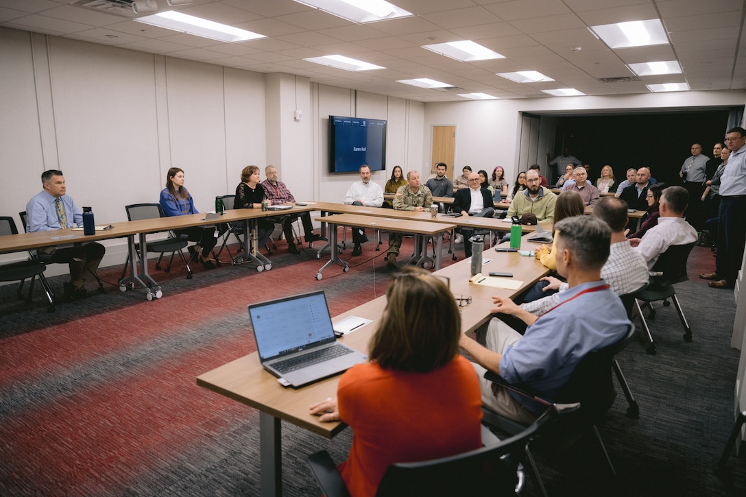 People sit at tables set up in U-shape around a conference room.