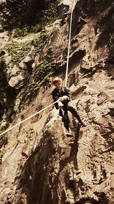 Girl in camo uniform comes down a cliff by rope.
