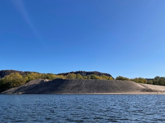 An island of sand with trees in the background and water in the foreground.