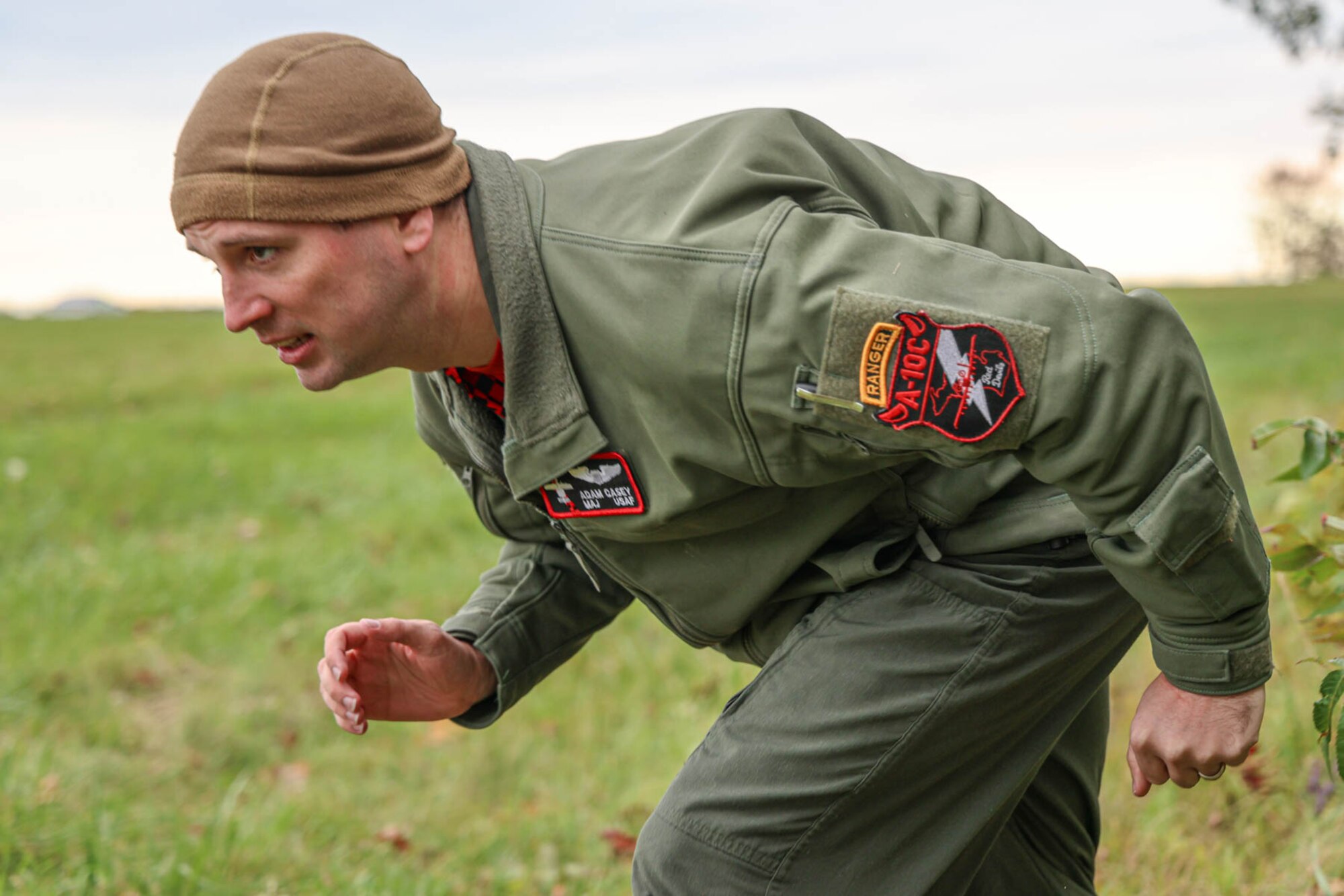 Airman, hunched over, wearing flight suit, running.