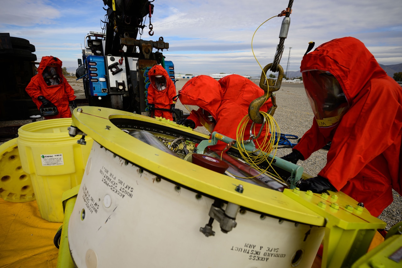 People in hazmat suits work to recover a missile guidance system.
