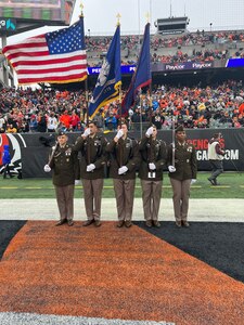 5 Army Soldiers stand serving the colors on the Bengals field. Two Soldiers are holding rifles, one Soldier is holding the American flag, one Soldier is holding the USAREC flag, and the final Soldier is holding the U.S. Army Recruiting and Retention College flag.