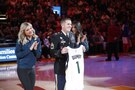 U.S. Army Soldier stands on an NBA court holding a personalized jersey. Two NBA cheerleaders stand on either side of him