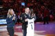 U.S. Army Soldier stands on an NBA court holding a personalized jersey. Two NBA cheerleaders stand on either side of him