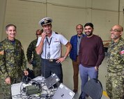 Lt. Commander Cameron Chapman, (center) capability integration manager, demonstrates MUOS voice calls from Major EJG Holland VC Armoury in Ottawa, accompanied by (left to right) Maj. Claude Provost, logistics support manager; Maj. Sam Myint, test and evaluation manager, Mr. Sadat Hussain ISS engineer, Mr. Rohit Malik systems engineer; and Capt. Balraj Pannu, test engineer.  Photo by George Blackwood