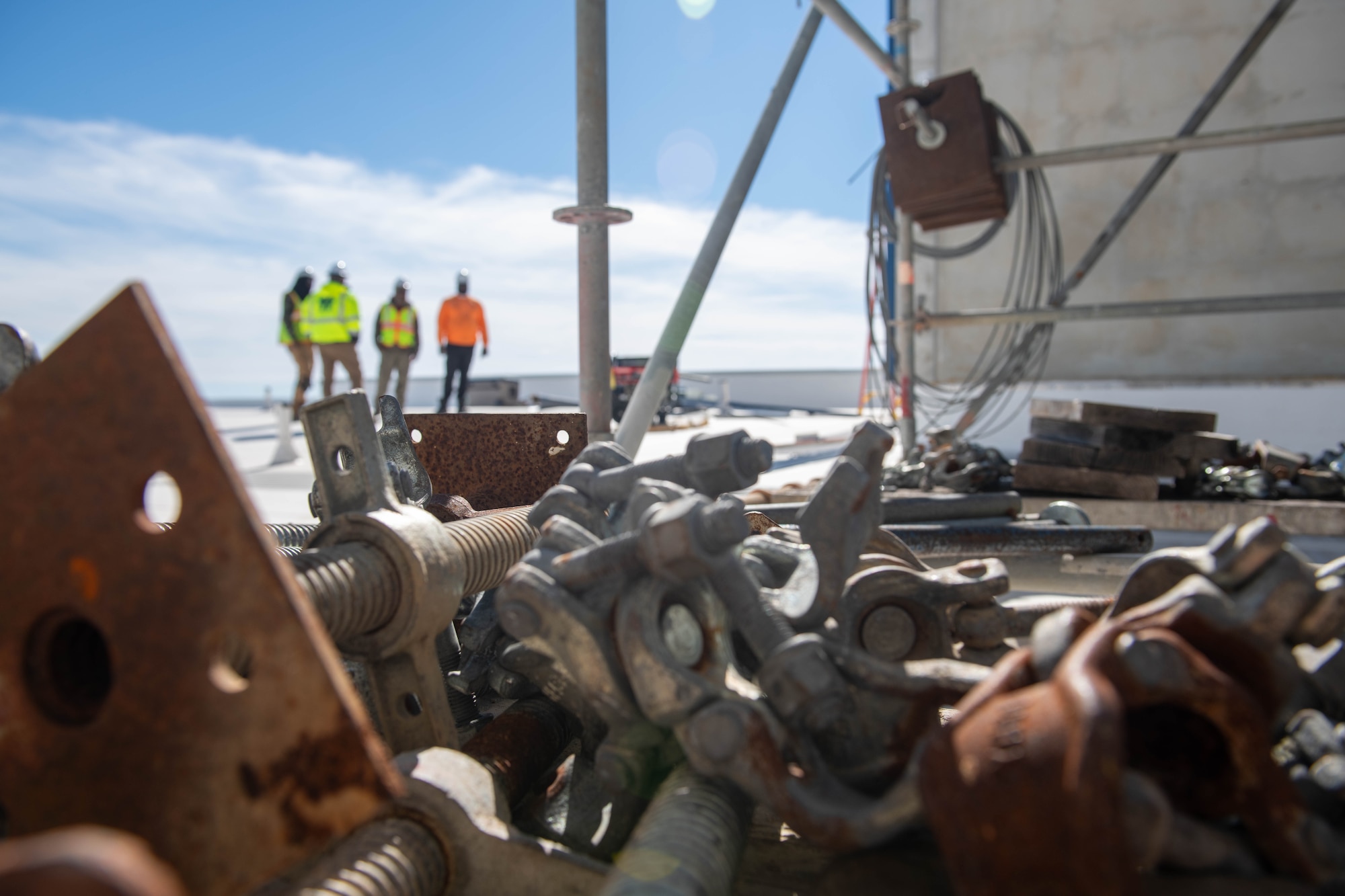A group of construction workers stand in the background with hardware in the foreground.