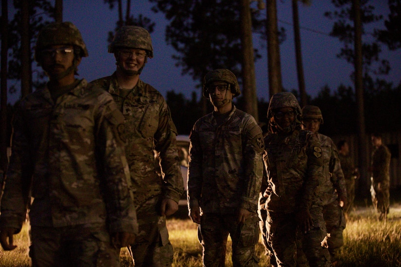 Soldiers prepare to board a Blackhawk helicopter. They are shown standing in line smiling for the camera.