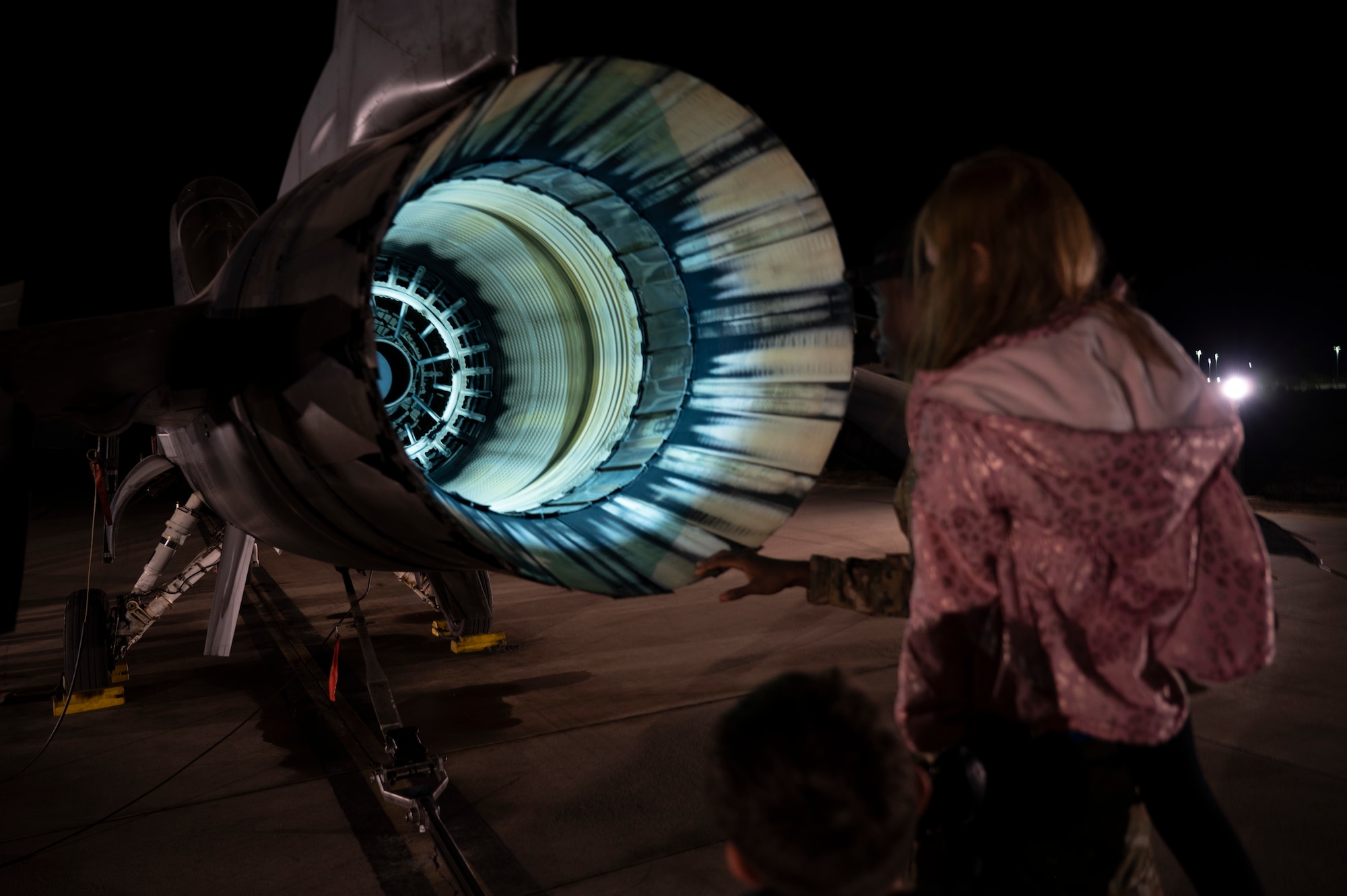 An Airman from the 311th Aircraft Maintanence Unit explains various parts of the F-16 Viper exhaust to a child at an afterburner operation at Holloman Air Force Base, New Mexico, Nov. 16, 2023. Afterburner operation occurs when raw jet fuel is injected into the engine augmenter, resulting in a long cone of fire out of the exhaust and generating twenty-four thousand pounds of thrust propelling the airframe. (U.S. Air Force photo by U.S. Air Force Airman 1st Class Michelle Ferrari)