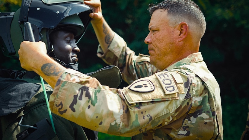 A soldier helps a foreign service member adjust a helmet.