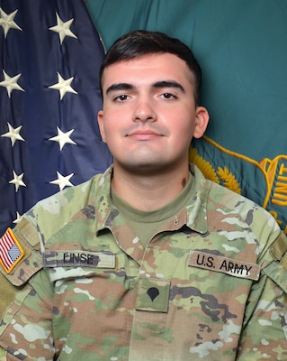 Man in U.S. Army uniform standing in front of two flags.