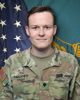 Man in U.S. Army uniform standing in front of two flags.