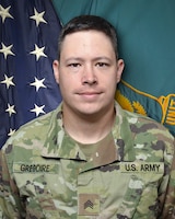 Man in U.S. Army uniform standing in front of two flags.