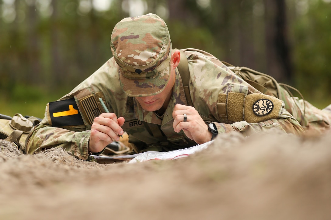 A soldier looks at some papers while lying on the ground.