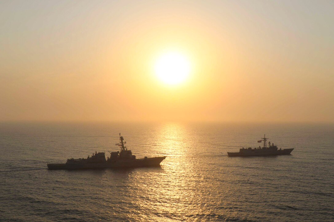 Two ships sail in formation under a sunlit sky.