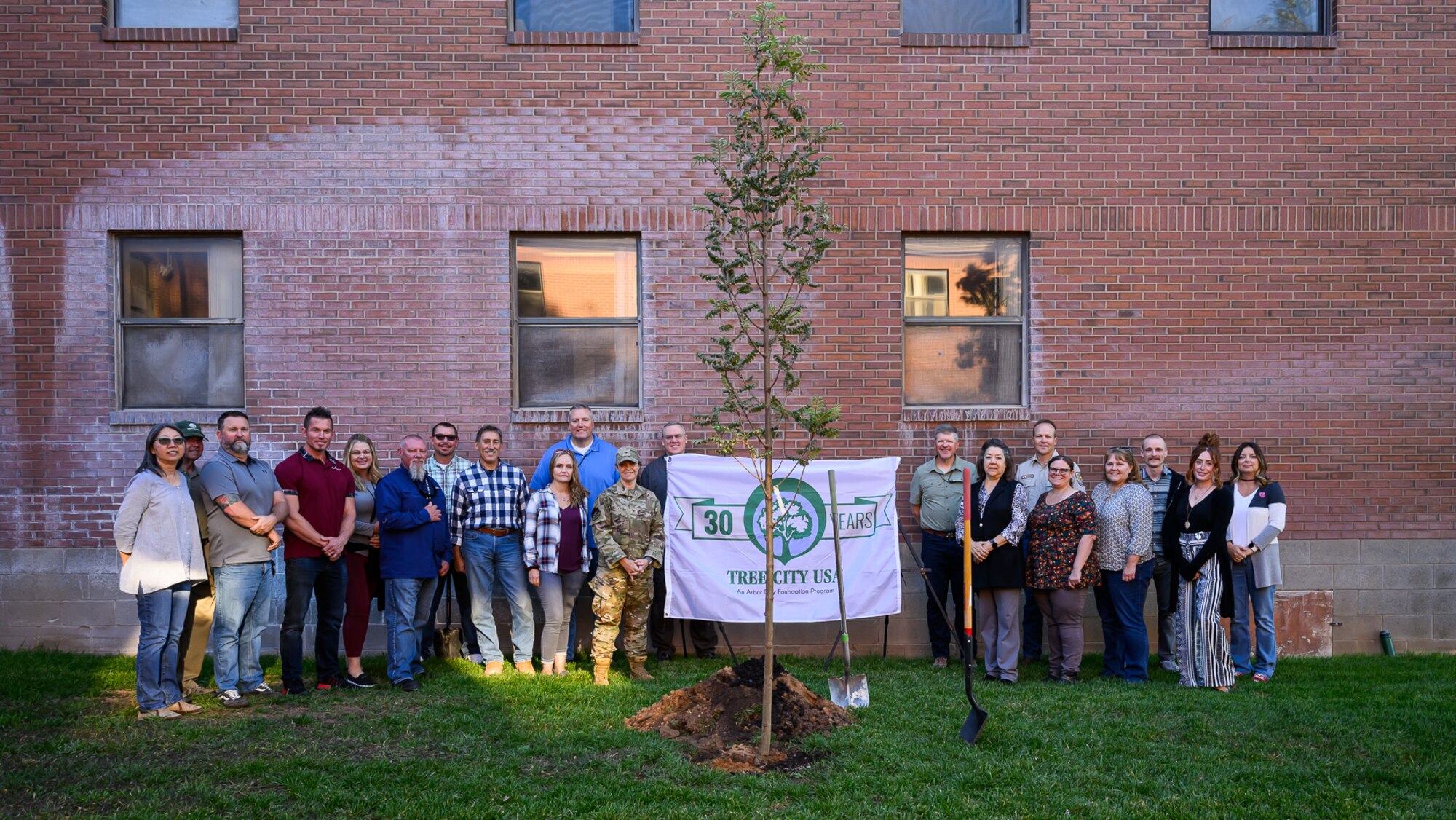 people gather in front of a brick building around a Tree City USA sign
