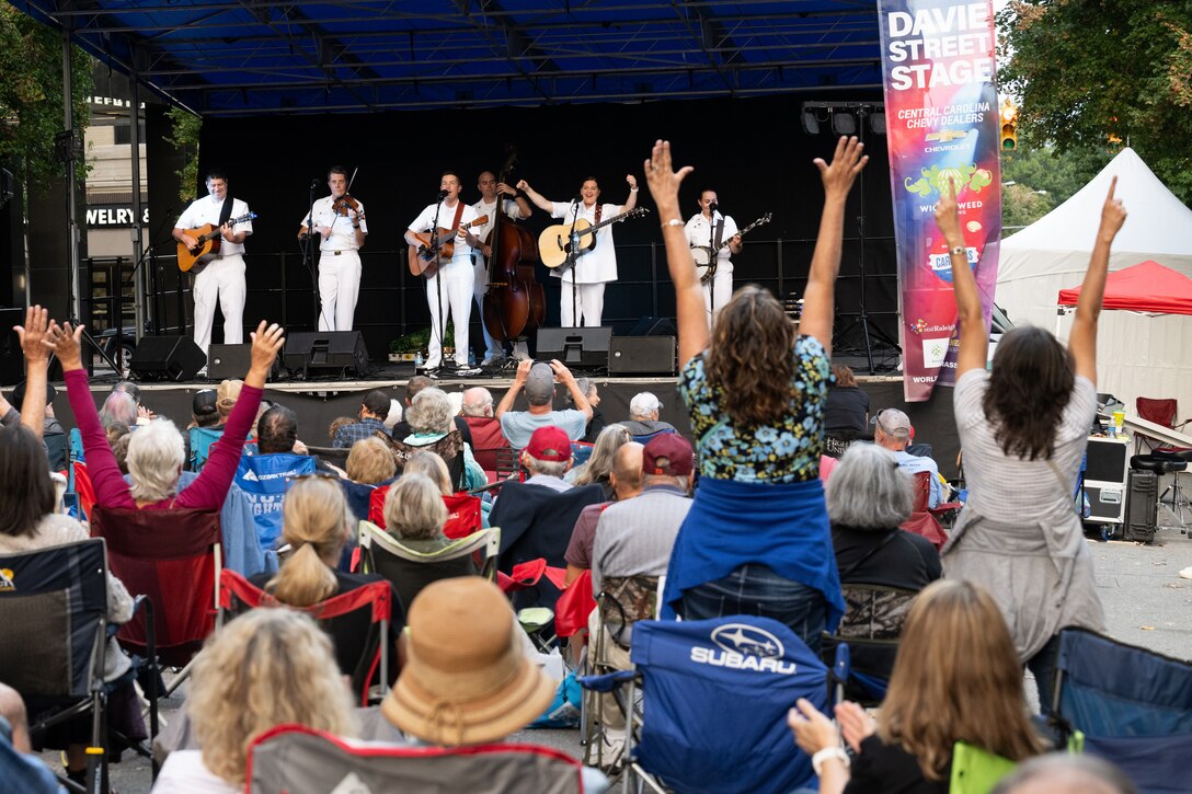 A group of musicians in white uniforms play for an audience.