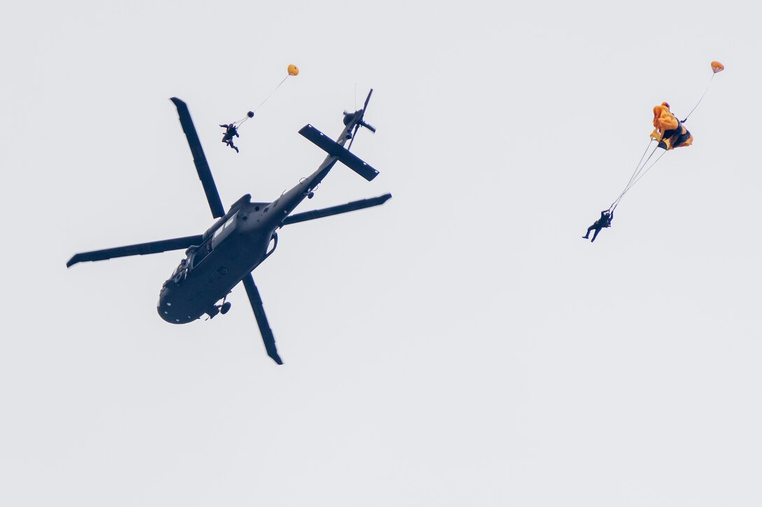 Two soldiers parachute from a helicopter.