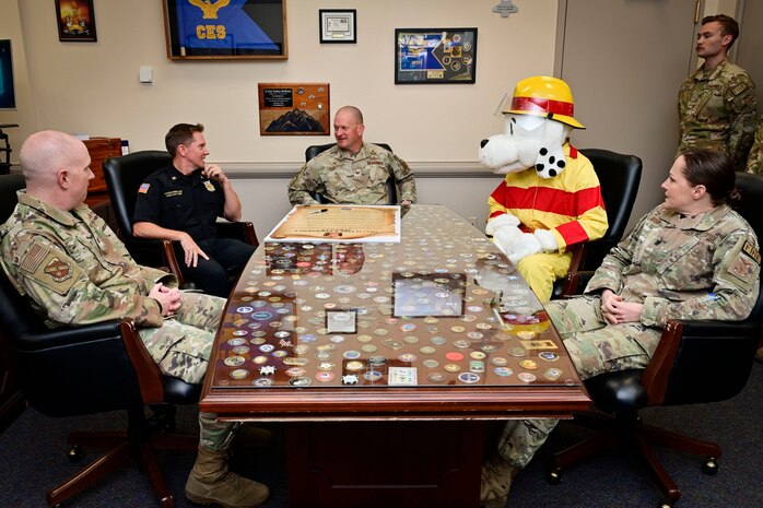 U.S. Air Force Col. Joshua DeMotts, 99th Air Base Wing commander, center, sits around a conference room table with members of the 99th Civil Engineering Squadron before signing the 2023 Fire Prevention Week Proclamation.