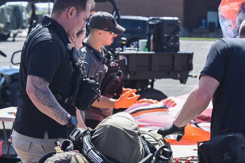 Service members stand over a simulated casualty on a stretcher during training.