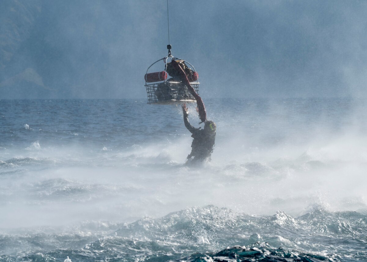 A U.S. Airman, training with the 68th Rescue Squadron, releases a basket of gear to be hoisted onto an aircraft off the coast of Calif., Sept. 13, 2023. The Airman remained in the water to assist multiple packages of gear into the aircraft. (U.S. Air Force photo by Airman 1st Class William Finn V)
