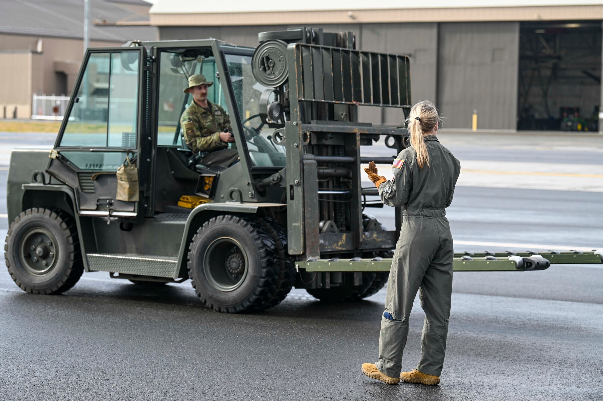 Airman 1st Class Sydnee Neal uses hand signals to guide Staff Sgt. Zach Reynolds who is driving the forklift