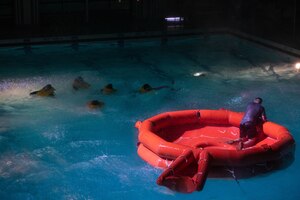 Airmen swim to a raft in a pool during water survival training.