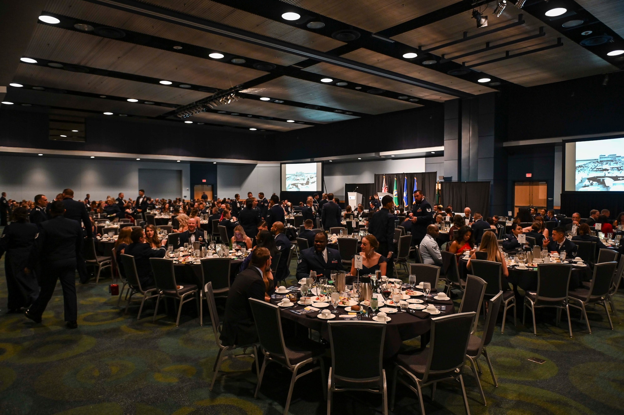 Airmen and their families sit at tables eating dinner and talking