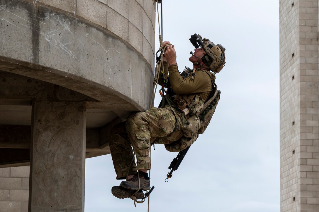 An airman uses ropes and cables to climb up a stone building.