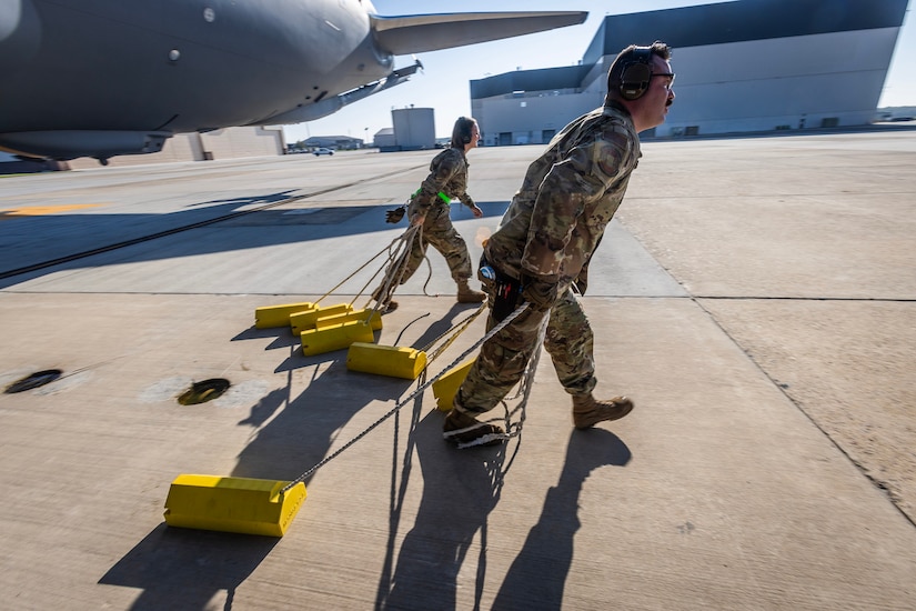 U.S. Air Force crew chiefs Senior Airman Robert Cort, front, and Master Sgt. Brittany Bounds with the New Jersey Air National Guard’s 108th Wing’s 141st Air Refueling Squadron, pull wheel chocks from a KC-46A Pegasus prior to a sortie at Joint Base McGuire-Dix-Lakehurst, New Jersey, Oct. 3, 2023. Seventeen pilots, boom operators, and crew chiefs made 108th history when they flew their first sortie on the KC-46A. (New Jersey National Guard photo by Mark C. Olsen)