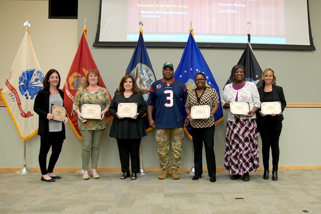 man in Army uniform and football jersey poses with women holding certificates