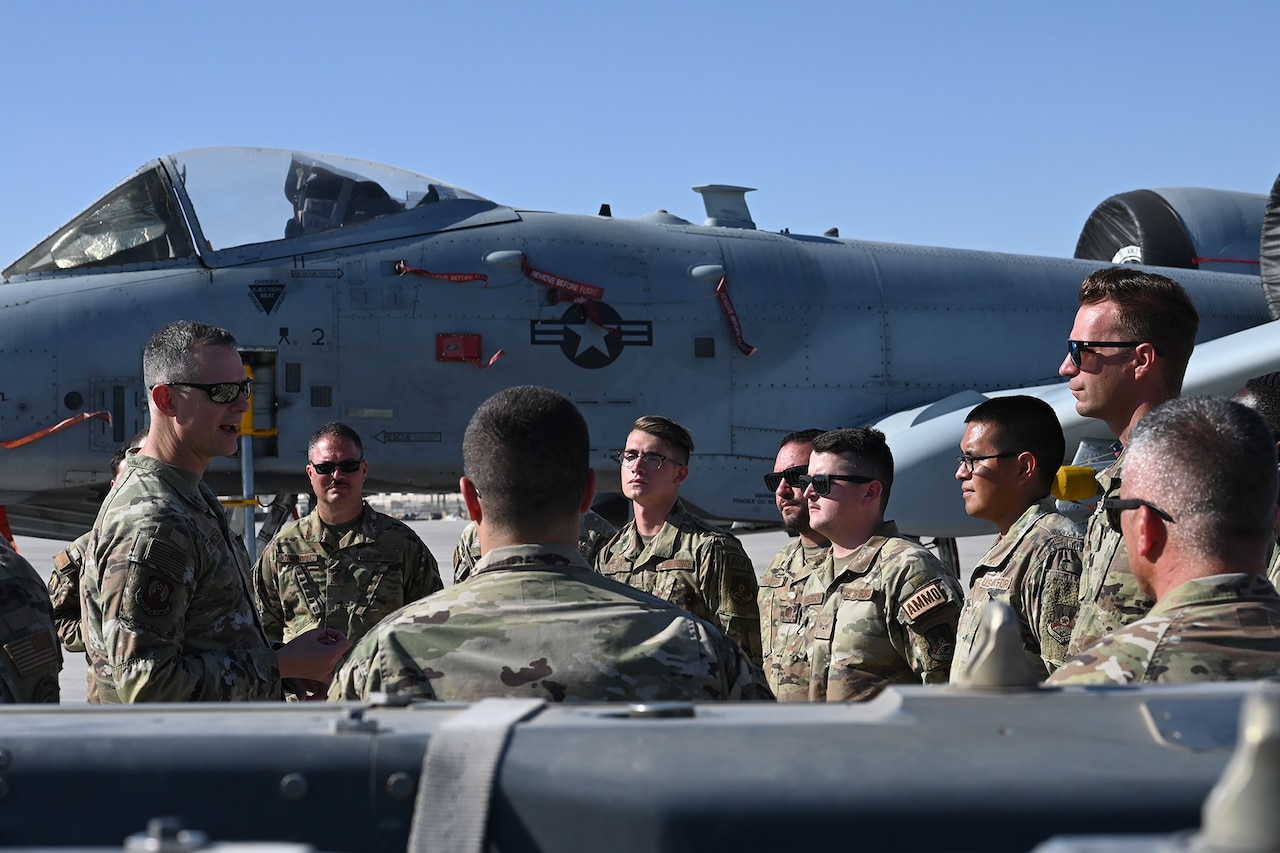 Uniformed service members stand in a group near an aircraft.