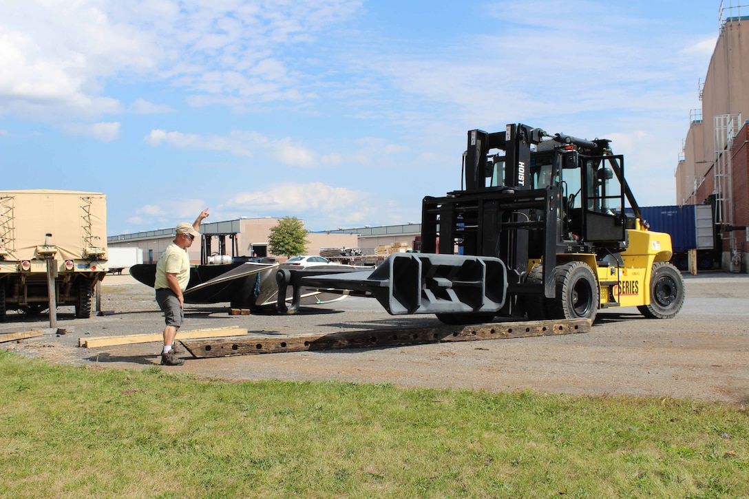 Man directing a forklift as it lifts a boat anchor onto wood planks.