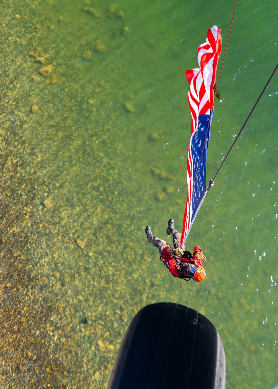 A sailor hoisted by an aircraft displays an American flag.