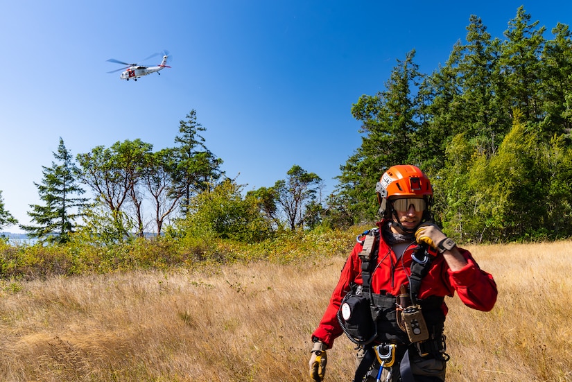 A sailor talks into a radio as an helicopter flies above.