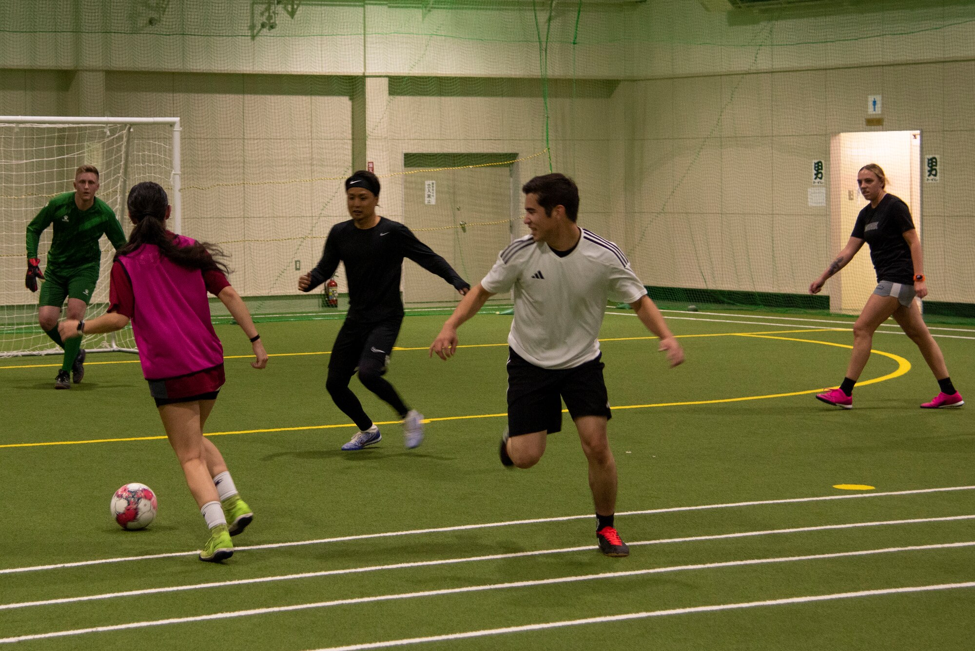 A group of players play soccer at an indoor soccer field.