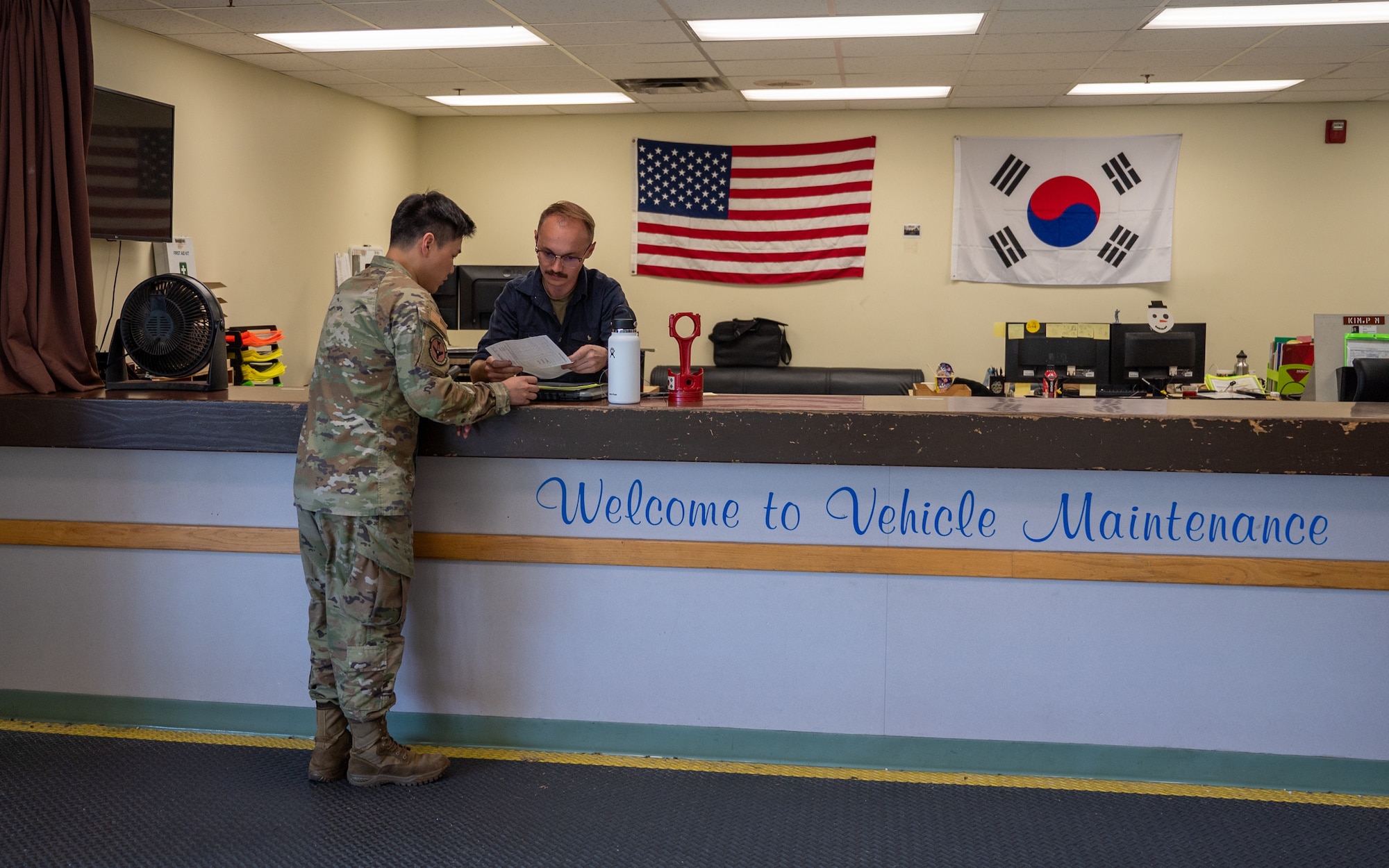 U.S. Air Force Staff Sgts. Byeongwoo Jung and Charles Donihue, both 51st Logistics Readiness Squadron vehicle maintenance mechanic technicians, discuss paperwork at the customer service desk at Osan Air Base, Republic of Korea, Sept. 8, 2023. Vehicle management services over 46 tenant units and validates their assets for functionality, safety, and resource management to ensure mission readiness for the 51st Fighter Wing. (U.S. Air Force photo by Staff Sgt. Kelsea Caballero)
