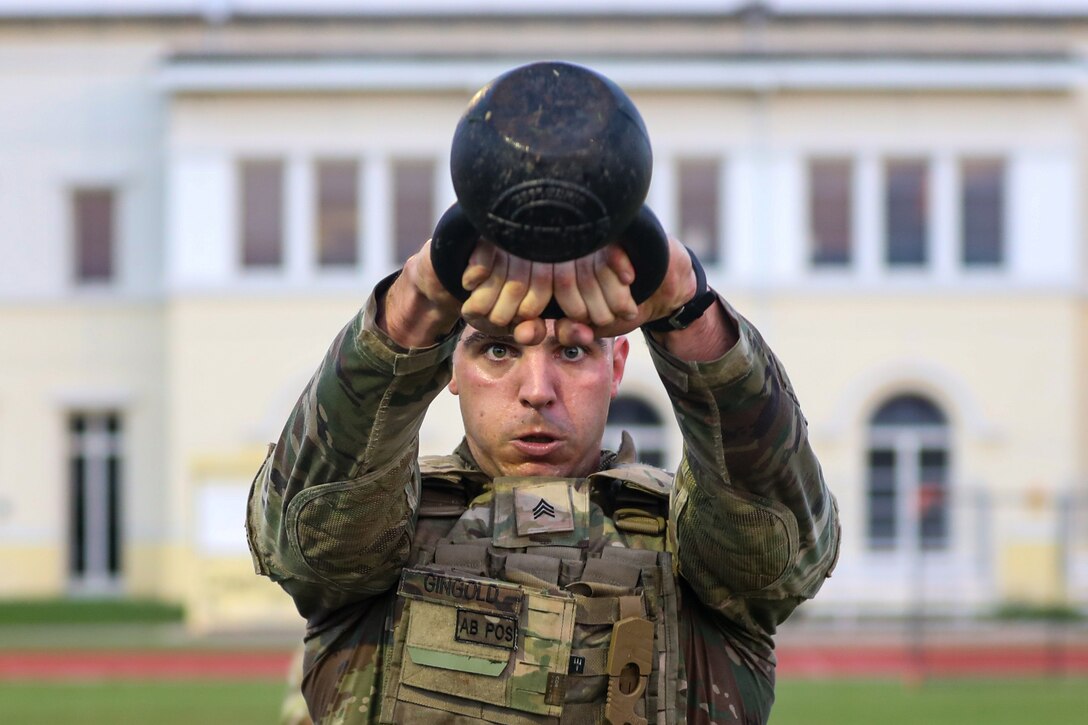 A soldier focuses as he swings a kettlebell.