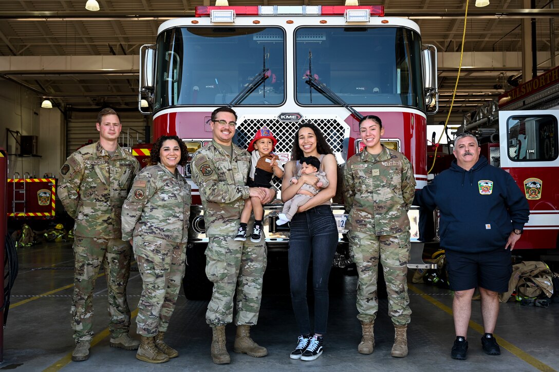 U.S. Air Force Senior Airman Derek Sutherland and his wife Tatiyanna Sutherland hold their children Daxtyn and Taytum, they are flanked by Senior Airmen Jacob La Plante, 28th Civil Engineer Squadron driver operator, left, Senior Airman Amari Alexander and Airman 1st Class Jewel Rodriguez, 28th Operational Medical Readiness Squadron aerospace medical technicians and Aaron Wilke, 28th CES fire captain at Ellsworth Air Force Base, Sept. 26, 2023.