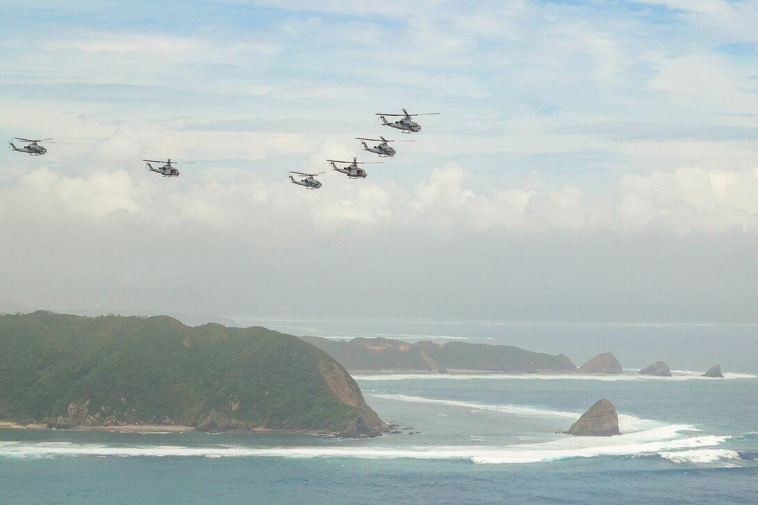 Six aircraft fly in formation over a coastal area.
