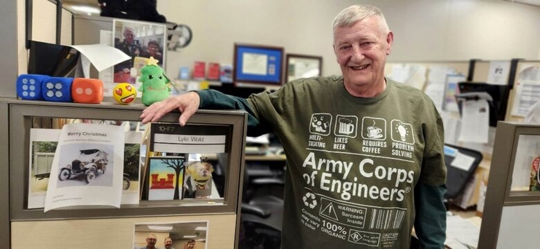 Lyle stands in front of his workstation wearing a USACE sweatshirt