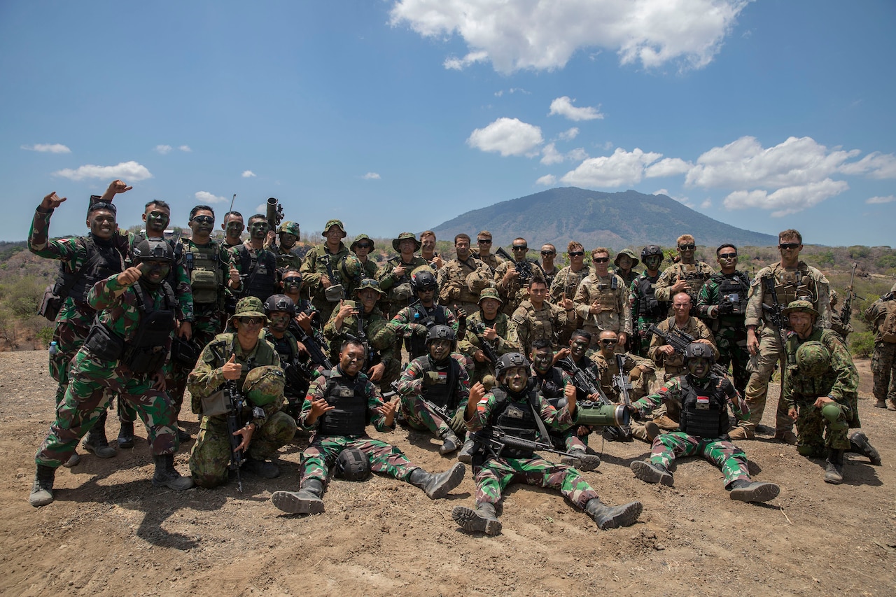U.S. and foreign soldiers wearing combat equipment pose together in the field.