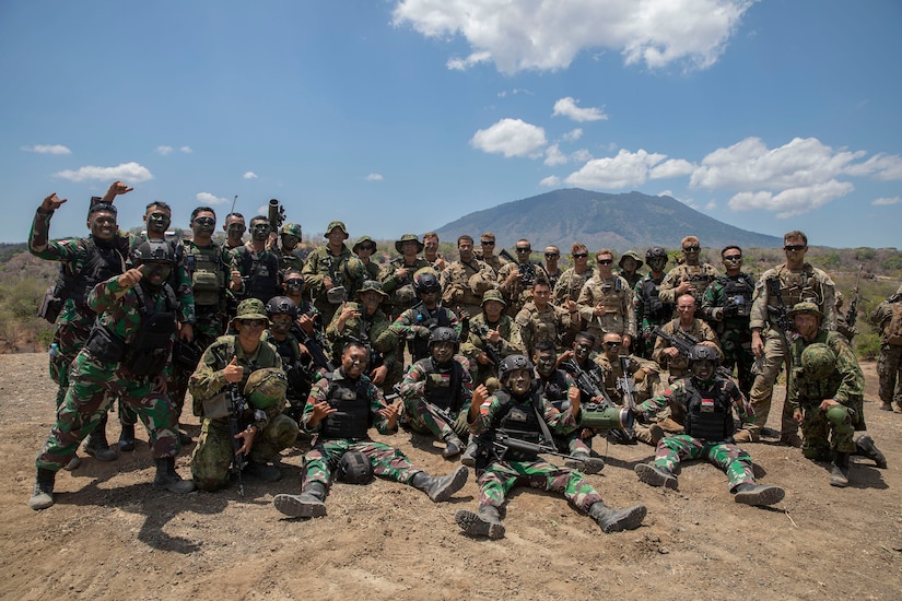 U.S. and foreign soldiers wearing combat equipment pose together in the field.