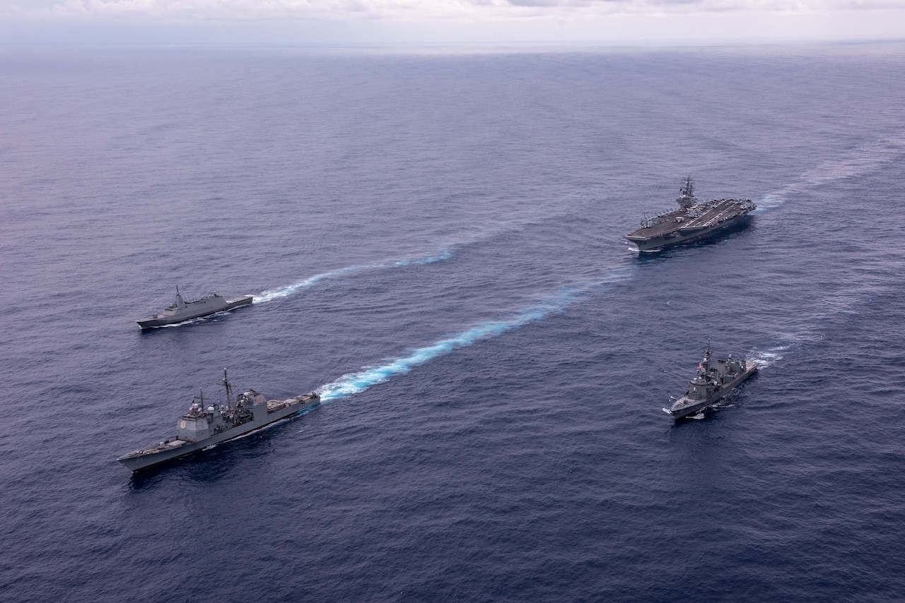 A group of U.S. and foreign military ships transit in open waters.